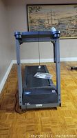Front view of treadmill showing running belt, frame, and manual on treadmill.