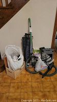 Full view of vacuum and accessories piled together including white bag and cardboard box near the unit