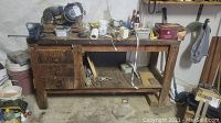 Full view of the wooden workbench showing drawers, open shelf, vise, bench grinder, and miscellaneous items on the surface.