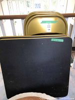 Two card tables with black tops and gold trim stacked upright beside four gold folding chairs