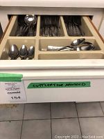 Drawer containing cutlery organized by type in plastic compartments showing patterned stainless steel forks, knives, spoons, and serving pieces.