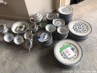 Overview of full dish set including stacked plates, bowls, spoons, teapot, and cups all in blue and white floral pattern.