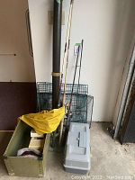 Four fishing rods standing upright with attached reels beside a black rod tube and two folded green wire mesh crab traps