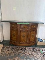 Full front view of wooden hall table with marble top in corner of room, showing wood grain and brass handles.