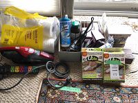 Overview of the lot items including handheld vacuum, toilet paper, Lysol wipes, power strip, cords, and boxes with supplements and adhesives.