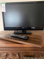 Front view of the black Insignia 26-inch LCD TV on a wooden surface with remote control placed in front.