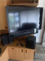 Insignia 46-inch flat-screen TV placed on corner shelf with accompanying Polk Audio speakers and subwoofer. Also includes remotes seen in front of equipment.