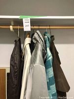 Four men's outerwear jackets and coats hung on a wooden rack, showing varied colors and materials.