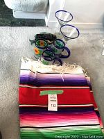 Photo showing Mexican-style striped woven blanket folded with three colorful decorative glass mugs nearby.