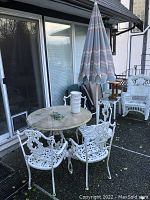 Full view of patio set on back deck against sliding glass door showing round table, four chairs and closed umbrella.