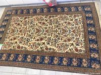 Full view of rectangular floral patterned area rug with a tan center field and blue borders including floral designs.