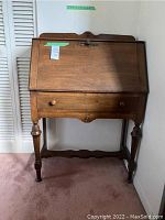Closed front view of the vintage secretary desk showing turned legs, single large drawer, and decorative back crest.