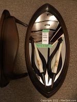 Faux wood shelf with oval mirror and two loop design black metal candle holders with white candles.