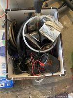 Top-down image of box containing various car accessories like hoses, thermostat, wiring, and a tester device.