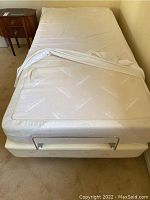Top view of single mattress in white zippered Tempur-Pedic cover on box spring with metal bar at foot