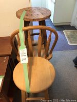 Image shows a wooden bar height kitchen chair with spindled back and rounded seat in front of an unfinished wooden stool with circular top.