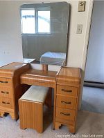 Front view of the wooden vanity with attached rectangular mirror, matching stool tucked under vanity, showing drawer handles and surface condition.