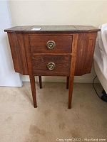 Front view showing two drawers with brass circular handles and tapered legs under a hinged top.