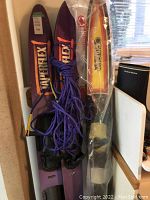 Photo showing both pairs of water skis with a blue tow rope coiled on top, and inflatable tubes in plastic packaging behind them.