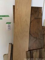 Light-colored plywood sheet and dark stained wood plank leaning against a white wall.