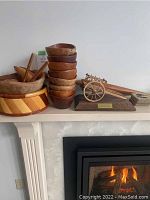 View showing stacked small wood bowls, large salad bowls, wooden sword behind, decorative wooden cart, and coasters on a shelf.