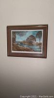 Full view of the framed lithograph on a wall showing the landscape artwork in natural oak and black-edged frame.