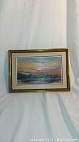 Front view of framed oil painting showing sunset over lake landscape with pink sky and dark treeline.
