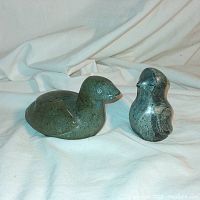 Front view of both soapstone bird sculptures: a longer Loon and a smaller standing Owl with signature visible.