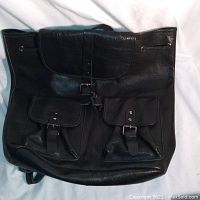 Front view of the black leather Hibou napsack showing the two front exterior pockets with buckles and the top flap.