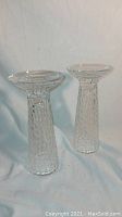 Pair of clear textured tall glass candlestands with jagged surface, shown standing side by side on white background.