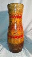 Full view of the tall ceramic vase showing the abstract geometric pattern in orange, red, yellow, and brown colors with textured glossy glaze.