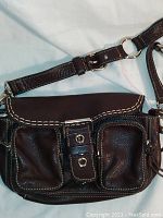 Front view of Roots brown leather saddlebag showing snap closure and two front zippered pockets with white stitching.