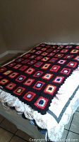 Full view of the vintage square knit blanket covering a bed, showing its overall design, colors, and size.