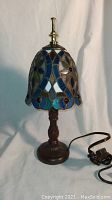 Full view of the lamp showing stained glass shade and carved metal base with cord and switch.