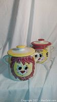 Photo showing both vintage ceramic cookie jars with lion and cat faces, each with two handles and lids.