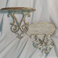 Pair of vintage wooden wall shelves with scrollwork support, painted white with gold overlay, showing paint loss and wear