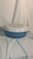 Side view of vintage blue Pyrex casserole with white garland and snowflake design, lid on.