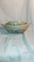 Side view of one Vintage Pyrex mixing bowl with blue floral pattern on cream base, showing decorative design and handles.