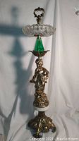 Full view of tall vintage ashtray showing marble base, metal angel figure, green glass element, faceted glass ashtray bowl and metal top handle