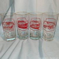 Front view of four clear vintage drinking glasses each featuring red TTC streetcar and bus designs with gold rims, arranged side by side