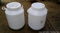 Two large white plastic barrels with screw top lids on a concrete floor, showing front and side views.
