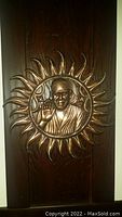 Front view of circular bronze or brass wall plaque showing detailed portrait relief of Guru Nanak surrounded by sunburst design mounted on dark wood.