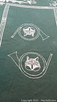 Close-up of central design showing two hunting horns each with detailed fox heads woven in white on green fabric.