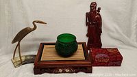 View of entire lot showing plant holder, green vase, crane sculpture, carved wooden wall hanging and decorative box