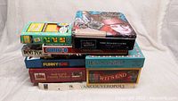 Photo showing stacked vintage board games including Vancouveropoly, Ginny-o, Alice in Wonderland, Dog Pile, Funny or Die, It's a Living, Awkward Family Photos, Wit's End.