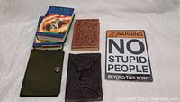 Top down view showing two copies of first Canadian edition Harry Potter and the Half Blood Prince, two leather notebook covers (green and dark brown with embossing), a vintage Adventures of Huckleberry Finn book, and a metal humorous sign.
