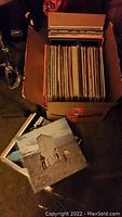 Box of vinyl records packed vertically in an Amazon box with some records displayed outside the box showing album covers.