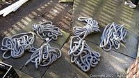 Six bundles of grey coated climbing rope coiled on the ground, varying thicknesses around 1 inch and 3/4 inch, lengths roughly 25 feet each.