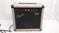 Front view of Fender R.A.D. guitar amplifier showing gray carpet covering and black front grille with Fender and R.A.D. logos, power cord visible on left side.