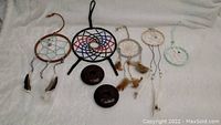 Top-down view of two brown Boma Gallery candle holders and five assorted dreamcatchers arranged on a white fabric surface.